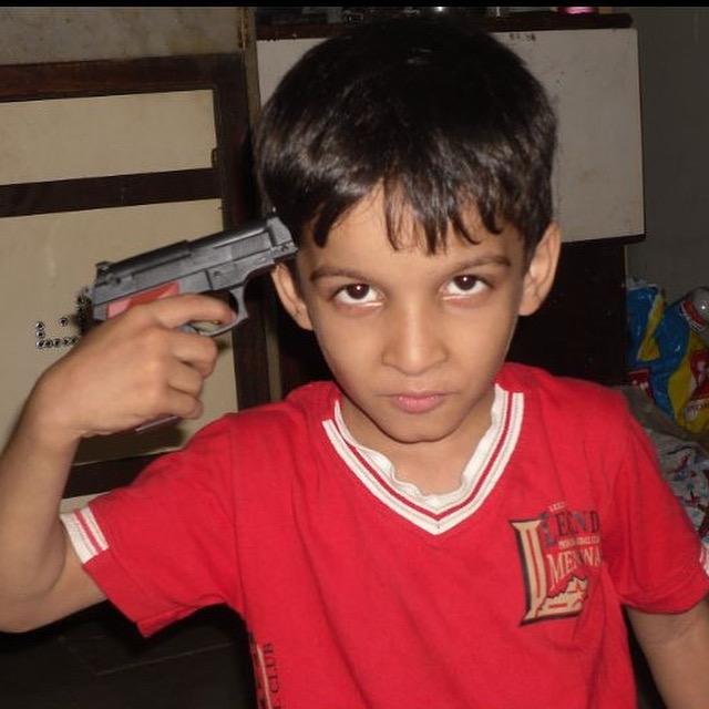Childhood photo in a red shirt with a pistol-shaped object held beside the head