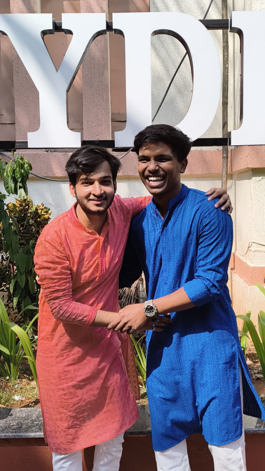 Two people smiling outdoors in red and blue traditional outfits